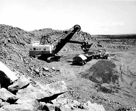 Large electric power shovels lift five cubic yards of taconite at a time and load it into forty-five ton side-dump trucks to be hauled from the mine to Reserve's coarse-crushing plants at Babbitt Minnesota, 1960