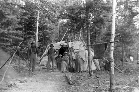 Indian family beside birch-bark wigwam and forest-side encampment near Ely Minnesota, 1890's