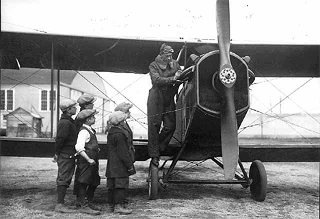 Boys examining an airplane at airport hangar, 1925