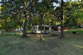 Photo of a camper parked in a campsite shaded by oak canopy.