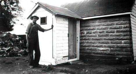 Joe Corrigan standing by the outhouse on farm, Apple Valley, Minnesota, 1951